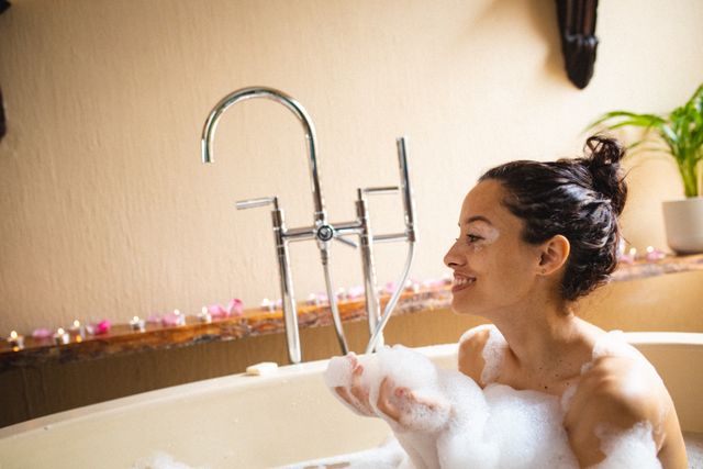 This image shows a smiling woman with vitiligo enjoying a relaxing bubble bath in a spa setting. The scene includes a bathtub filled with bubbles, soft lighting, and candles, creating a tranquil and pampering atmosphere. Ideal for use in wellness and spa promotions, self-care articles, body positivity campaigns, and lifestyle blogs.