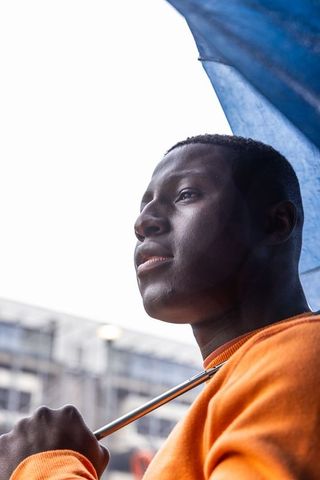 Holding umbrella and gazing upward urban portrait in orange sweatshirt under gray sky