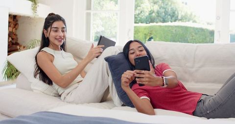 Friends enjoying relaxed time with gadgets in sunlit living room