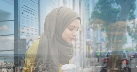 Asian Woman in Hijab Enjoying Coffee Amidst Urban Cityscape