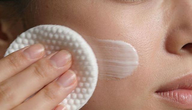 Applying moisturizer with cotton pad on asian woman cheek closeup skin care glow routine