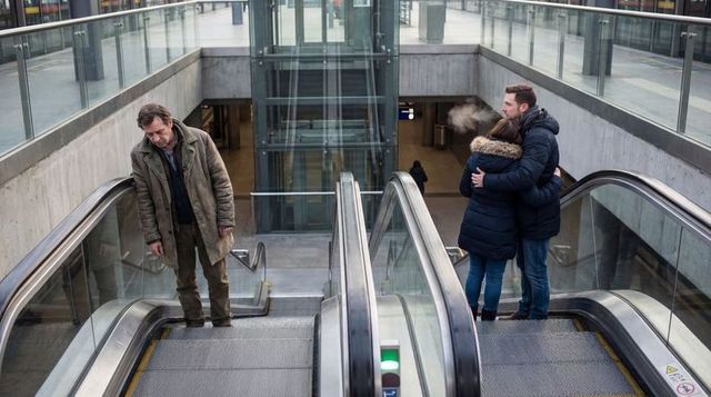 Embracing couple on subway escalator with lonely man descending at urban transit concourse