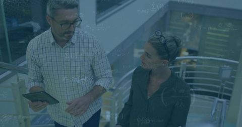 Colleagues discussing strategy while walking up modern office staircase holding tablet