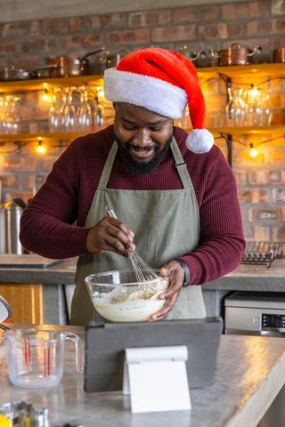 African american baker whisking holiday batter wearing santa hat olive apron cozy kitchen
