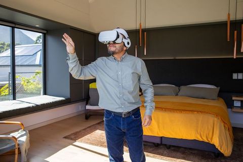 Mature asian man using vr headset in sunlit modern bedroom exploring virtual reality