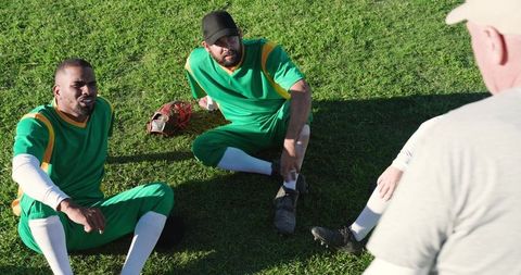 Baseball teammates listening to coach on grass field during practice break