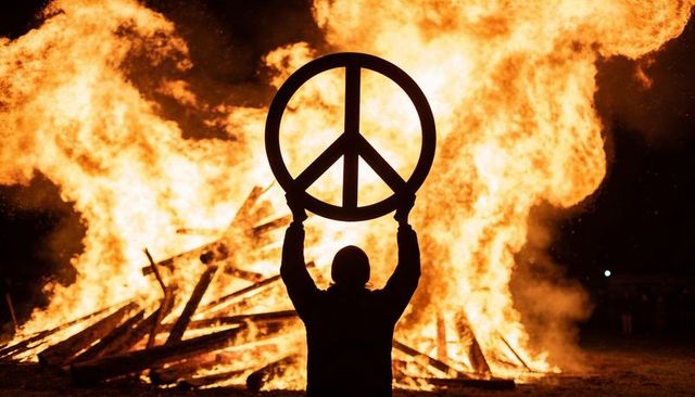 Silhouette raising peace symbol over bonfire at night - protest, ritual, activism