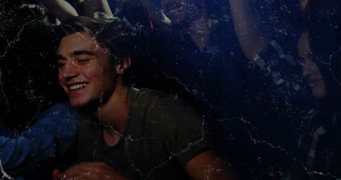 Young man smiling and leaning in crowded nightclub under blue lights and raised hands