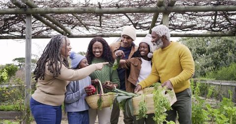 Multigenerational family harvesting homegrown vegetables in backyard garden, sharing joy