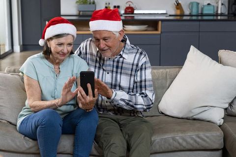Senior Couple with Santa Hats Using Smartphone on Couch at Home