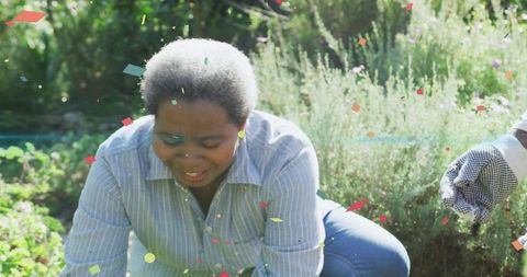 Senior woman joyfully gardening in flower bed with confetti
