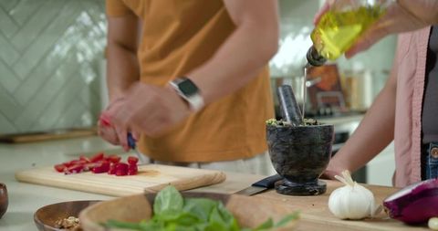 Diverse couple chopping red peppers and pouring olive oil while preparing fresh meal