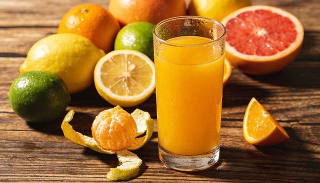 Fresh orange juice in dewy glass with assorted citrus fruits on rustic wood tabletop