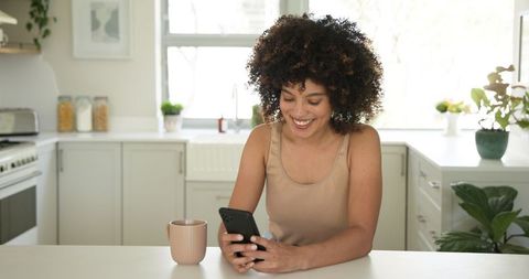 Cheerful Woman Using Smartphone in Bright Kitchen