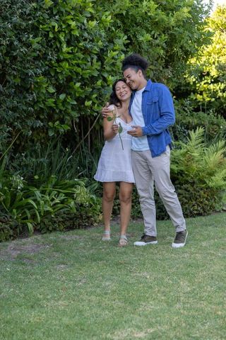 Young couple sharing romantic moment in sunlit garden, woman holding white rose