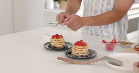 Sprinkling Powdered Sugar Over Pancake Stacks on Kitchen Counter