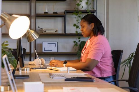 African american woman working on laptop in modern coworking space with plants and lamp