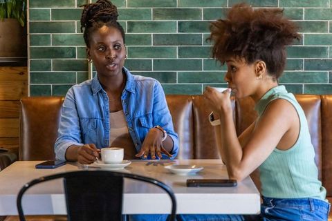 African american women chatting over coffee in urban cafe, denim and mint green outfits
