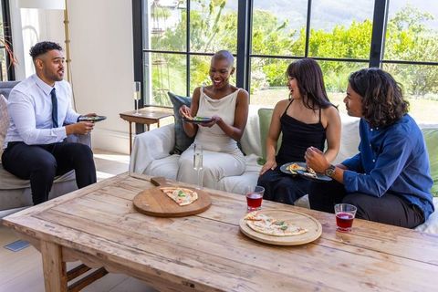 Multicultural friends laughing and sharing pizza on sofa during casual indoor gathering