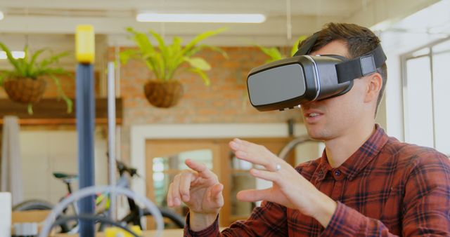 Young man exploring virtual environment with VR headset in a contemporary office space. Presents innovative and immersive technology use in the workplace. Use in articles or promotions about cutting-edge tech, workplace innovation, or interactive gadgets.