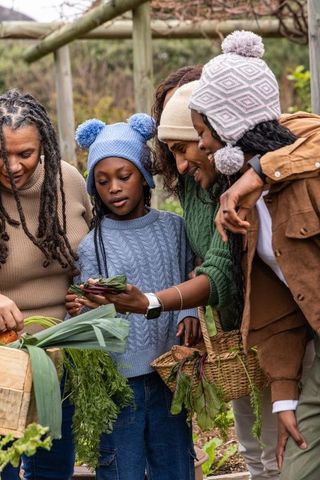 Multigenerational black family harvesting and examining fresh vegetables in backyard garden