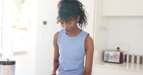 Sunlit modern kitchen african american woman preparing smoothie with personal blender