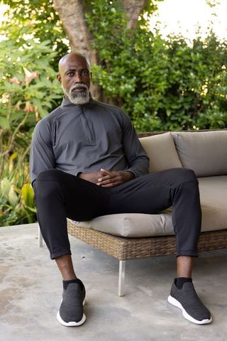 Senior man relaxing on wicker sofa in garden wearing athletic leisurewear and slip-ons