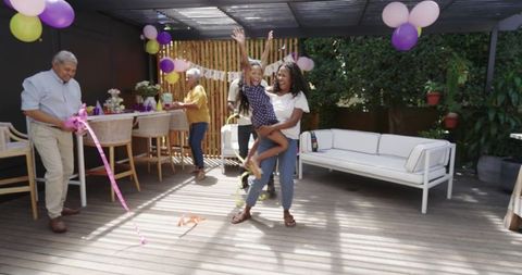 Multigenerational diverse family celebrating on backyard pergola deck with colorful balloons
