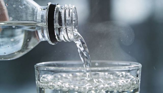 Macro pouring sparkling water from bottle into glass; bubbles, condensation, reflections
