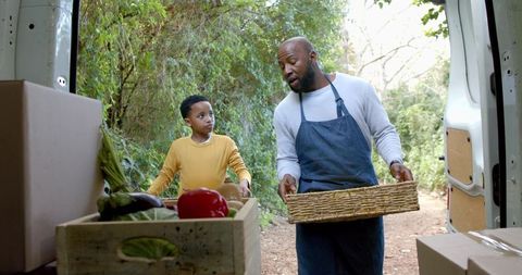 African american father and son unloading fresh farm produce from van in woodland