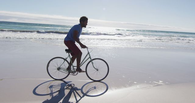 African american man smiling and riding bike on the beach - Download Free Stock Photos Pikwizard.com