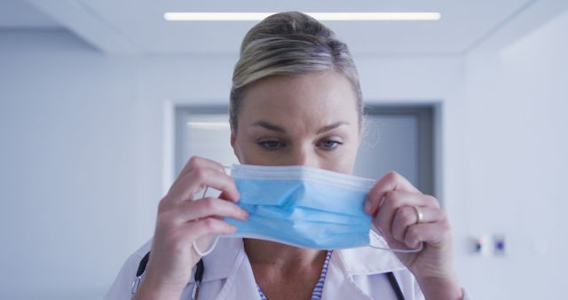 Female doctor in a hospital putting on a surgical mask. Ideal for content about healthcare safety, medical professions, hospital environments, and COVID-19 precautions. Useful for articles, blogs, and educational materials focused on medical practices and frontliners.