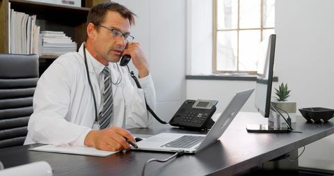 Physician Using Landline While Working at Desk in Clinic Office