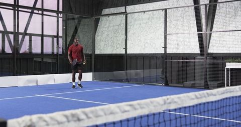 Athletic man playing padel tennis on modern court with glass wall