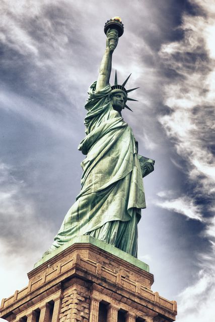 This image depicts a striking view of the Statue of Liberty set against a dramatic sky with clouds. Ideal for use in travel brochures, educational materials, and articles highlighting American landmarks, history, and tourism attractions.