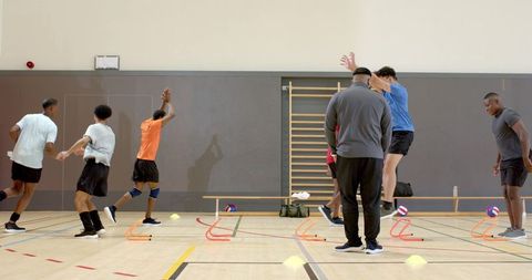 Multiethnic male volleyball team training agility drills with hurdles, cones and coach