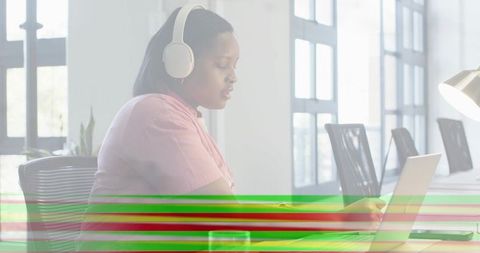 Woman wearing headphones working on laptop in bright coworking space with color banding