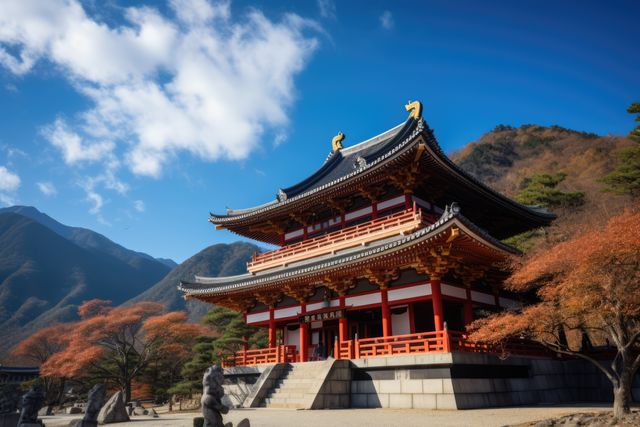This stock image features a historic temple adorned with classic Japanese architecture during autumn. Vibrant foliage surrounds the sacred building, enhancing its serenity and timeless beauty. The blue sky and mountains create a stunning backdrop, making this image useful for travel brochures, culture websites, and scenic calendars. Ideal for those highlighting Japan’s rich history, cultural heritage, and natural beauty.
