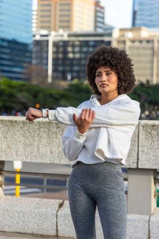 Urban athlete checking fitness tracker and stretching before morning run on riverside bridge