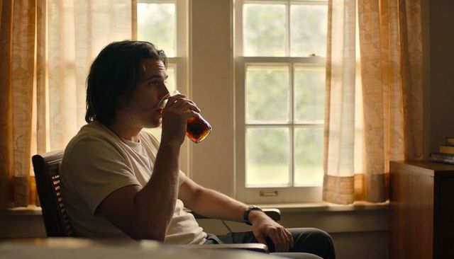 Man sipping iced tea from amber glass by window, contemplative moment in minimalist home