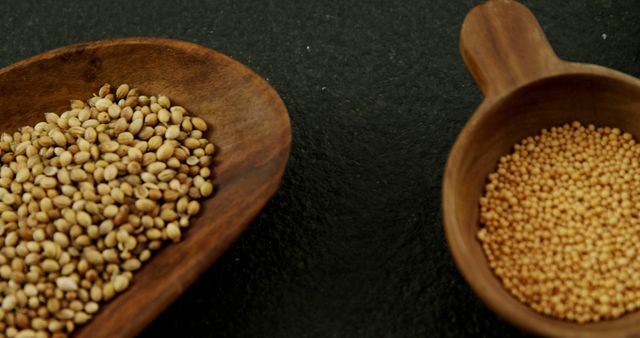 Two wooden bowls on a dark surface contain different types of grains, one with larger beige seeds and the other with smaller yellow seeds, with copy space. These grains are essential ingredients in various cuisines and represent healthy, plant-based sources of nutrition.