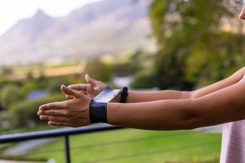 Female extending forearms over balcony railing wearing black cuff and watch, mountain view
