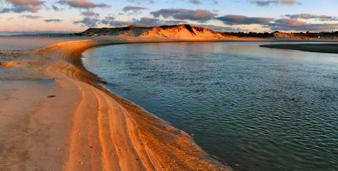 Golden curved sandbar leading to calm tidal lagoon with dune reflections at sunset