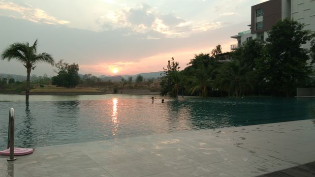 Peaceful sunset casting a warm glow over a modern swimming pool surrounded by lush landscape and distant hills. Ideal for promotions of retreats, vacation homes, relaxation themes, or leisure activities.