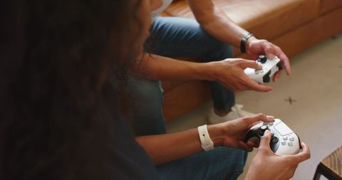 African couple playing video games together on leather sofa with white controllers