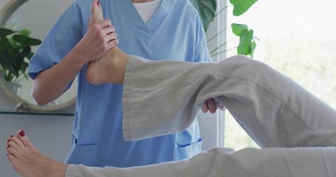 Physiotherapist stretching patient's leg for mobility rehabilitation in bright clinic