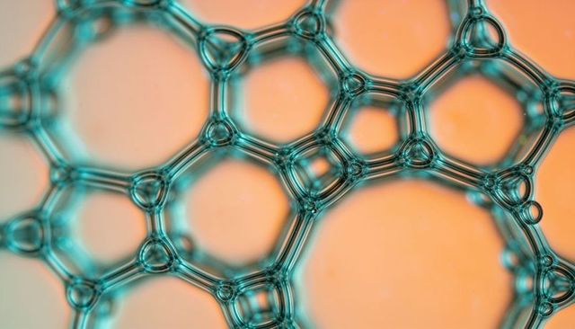 Teal soap film network forming honeycomb bubbles on orange backdrop macro abstract texture