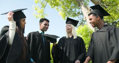 Happy multiracial friends celebrating graduation outdoors