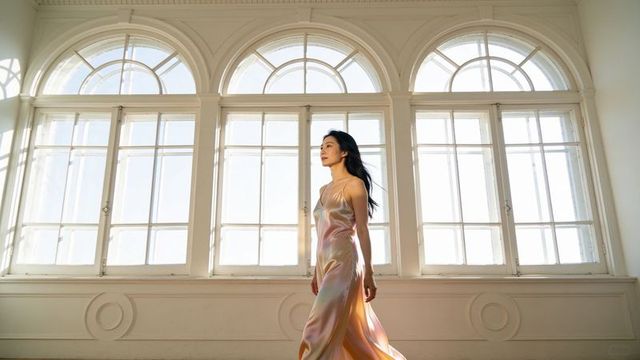 Walking asian woman in iridescent satin slip dress in elegant room with arched windows