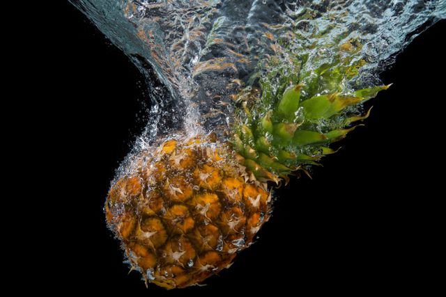 Pineapple making a splash as it plunges into clear water against a dark background, perfect for advertising fresh produce, tropical fruit beverages or promoting healthy eating. Great for use in food blogs, diet articles, or web banners promoting fruit products.